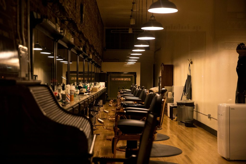 Dimly lit barbershop with vintage black chairs lined in a row against a long counter, mirrors reflecting soft light from overhead lamps, evoking a nostalgic feel.